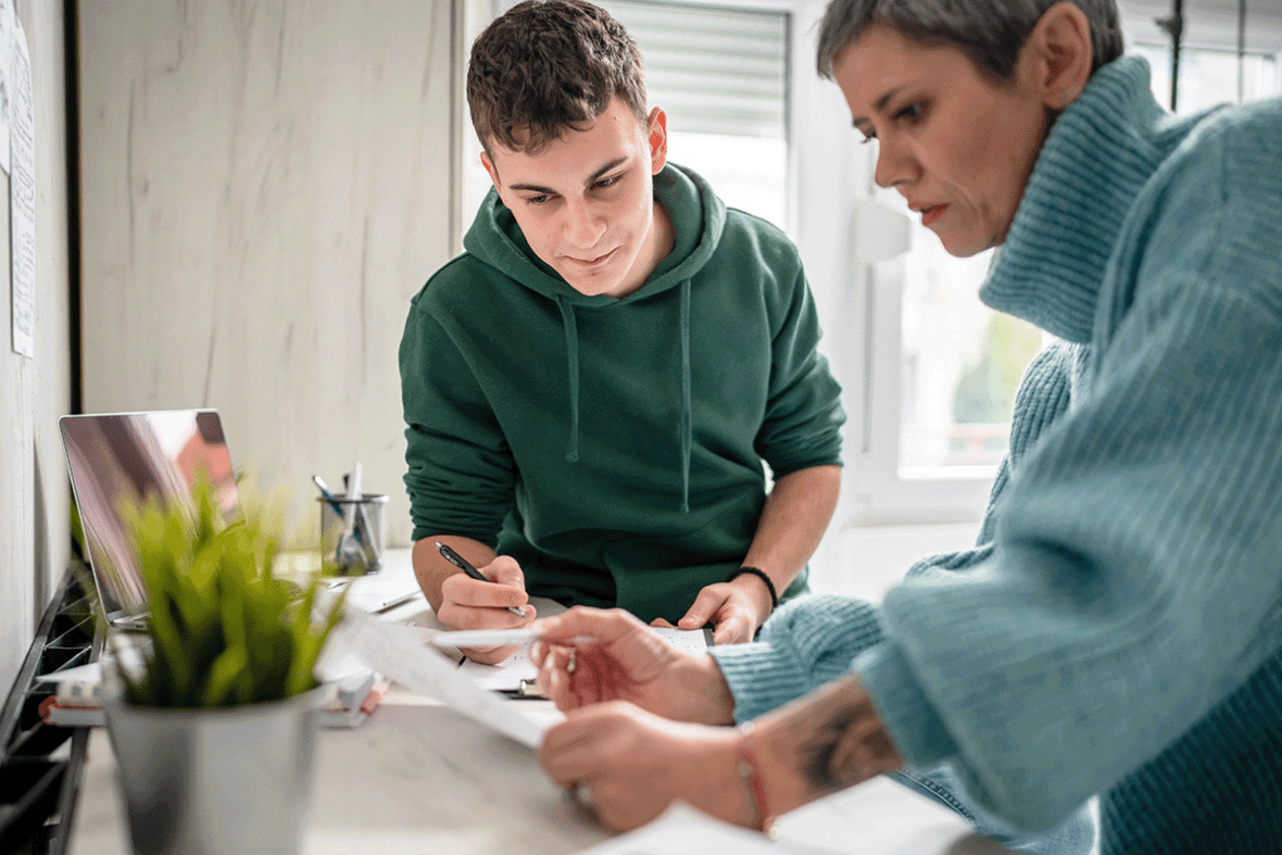 a teenage student fills out a form with the help of his mother