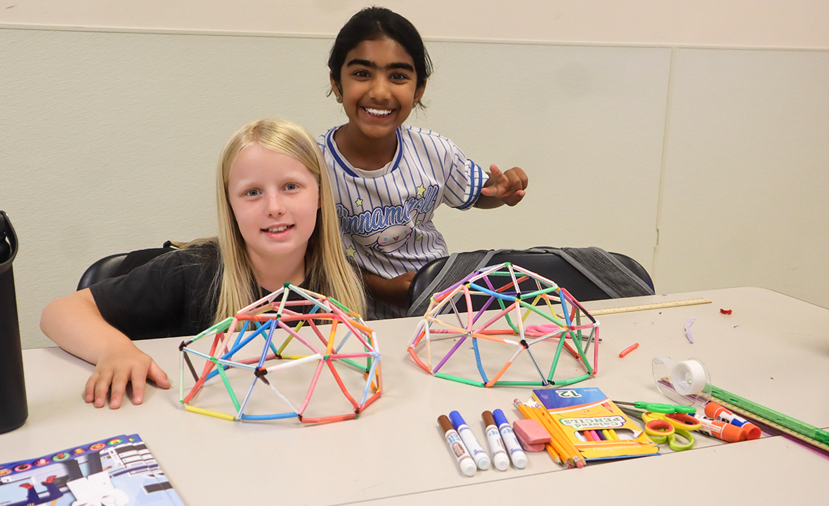 Two students smile while displaying colorful geometric dome models they built from straws and connectors.