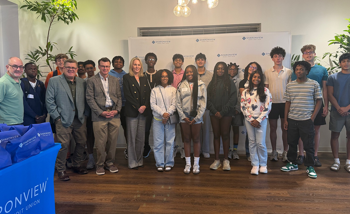 Group of students and adults posing together for a photo in front of a branded backdrop.